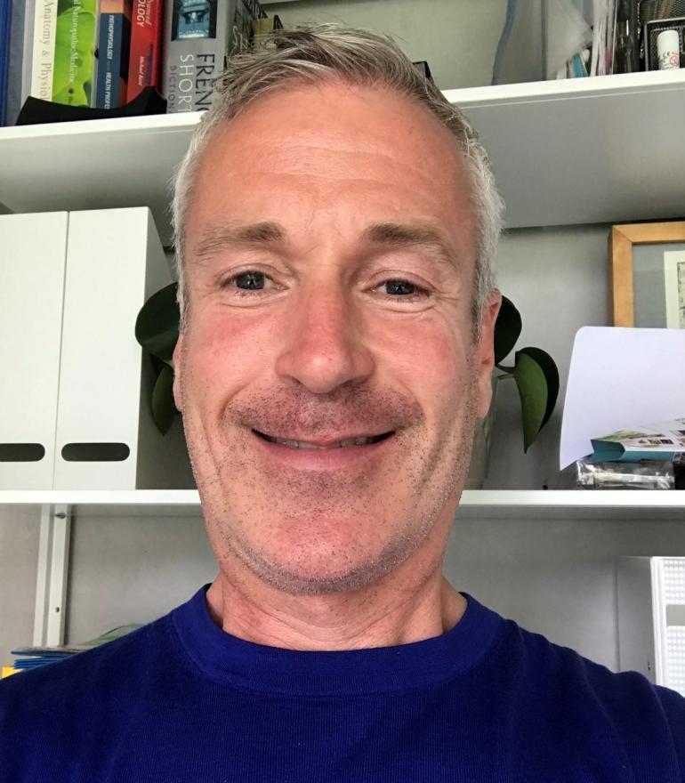 Image of Conleth Teevan smiling directly at camera in front of bookshelves