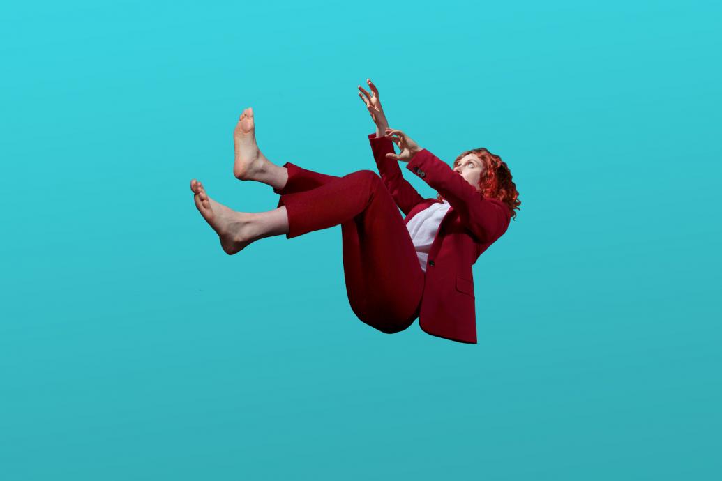 A barefoot woman in a red suit falls through a pure blue space