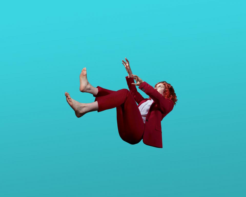 A barefoot woman in a red suit falls through a pure blue space