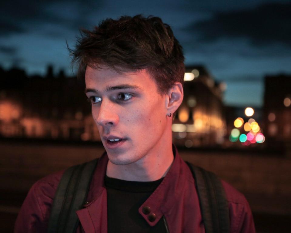 Patchwork, a man looks to the side in an urban space at twilight
