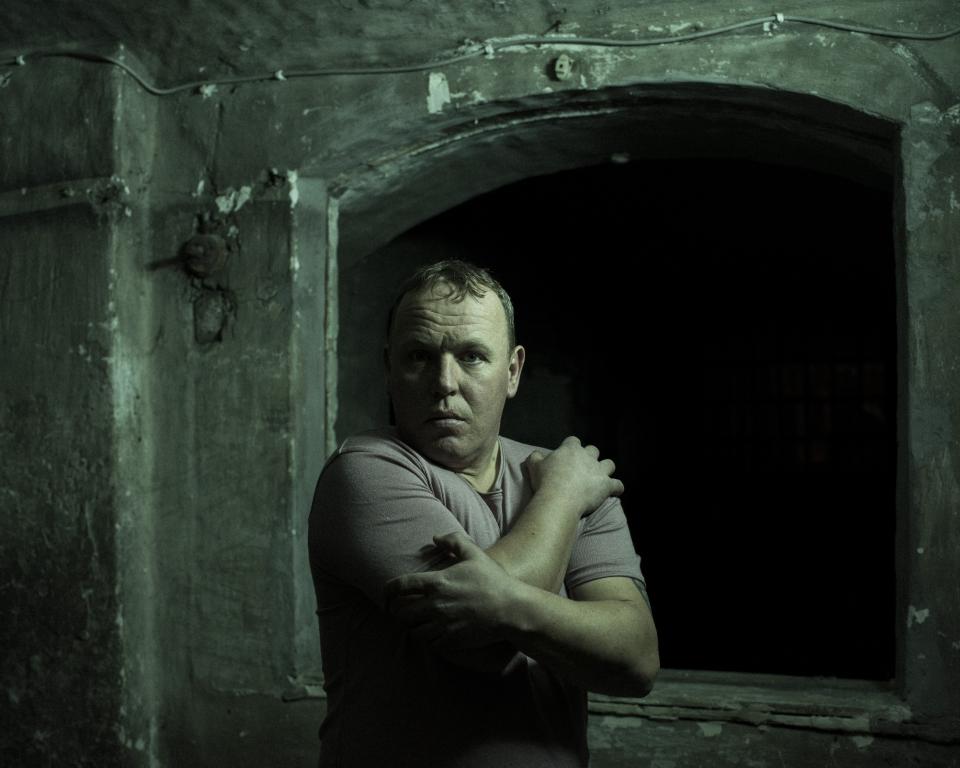 A man wraps his arms around himself in a dark room