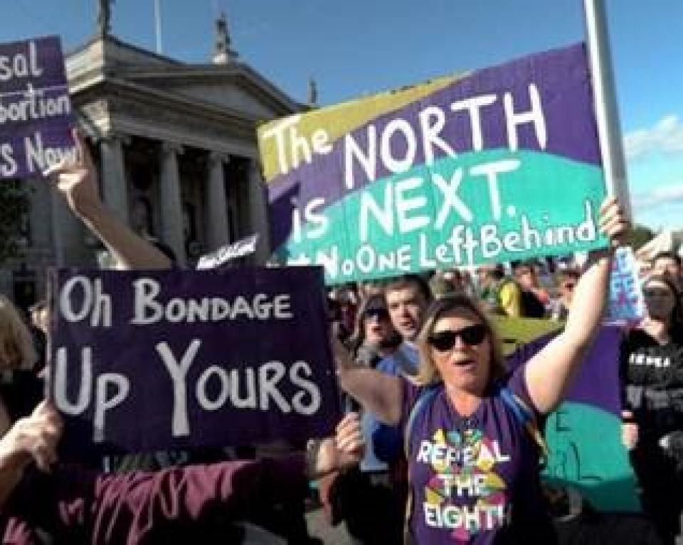 Woman demonstrating outside GPO, holding 'The North is Next' signs