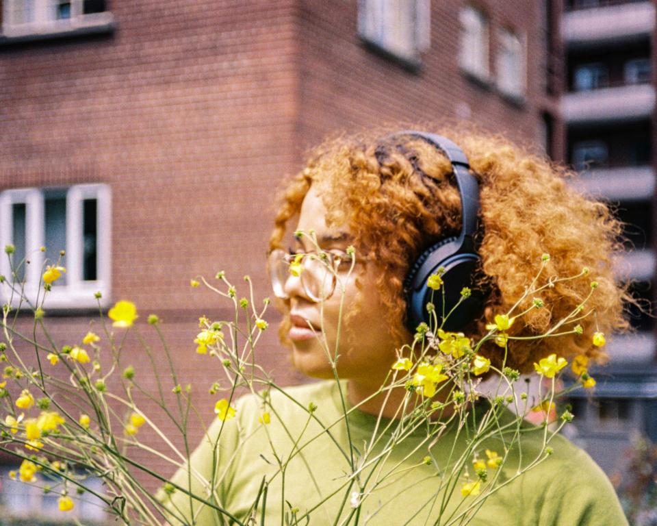 Woman with headphones by a yellow flowered bush