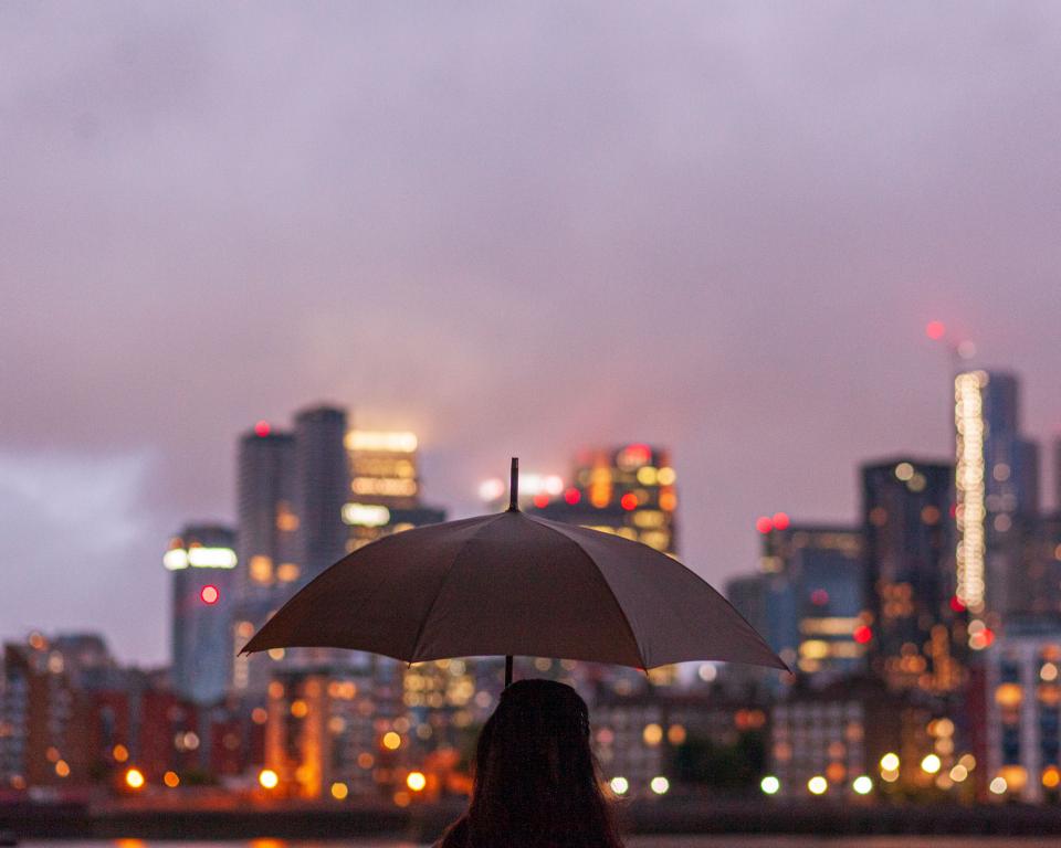 Person holding a umbrella facing dusky city lights