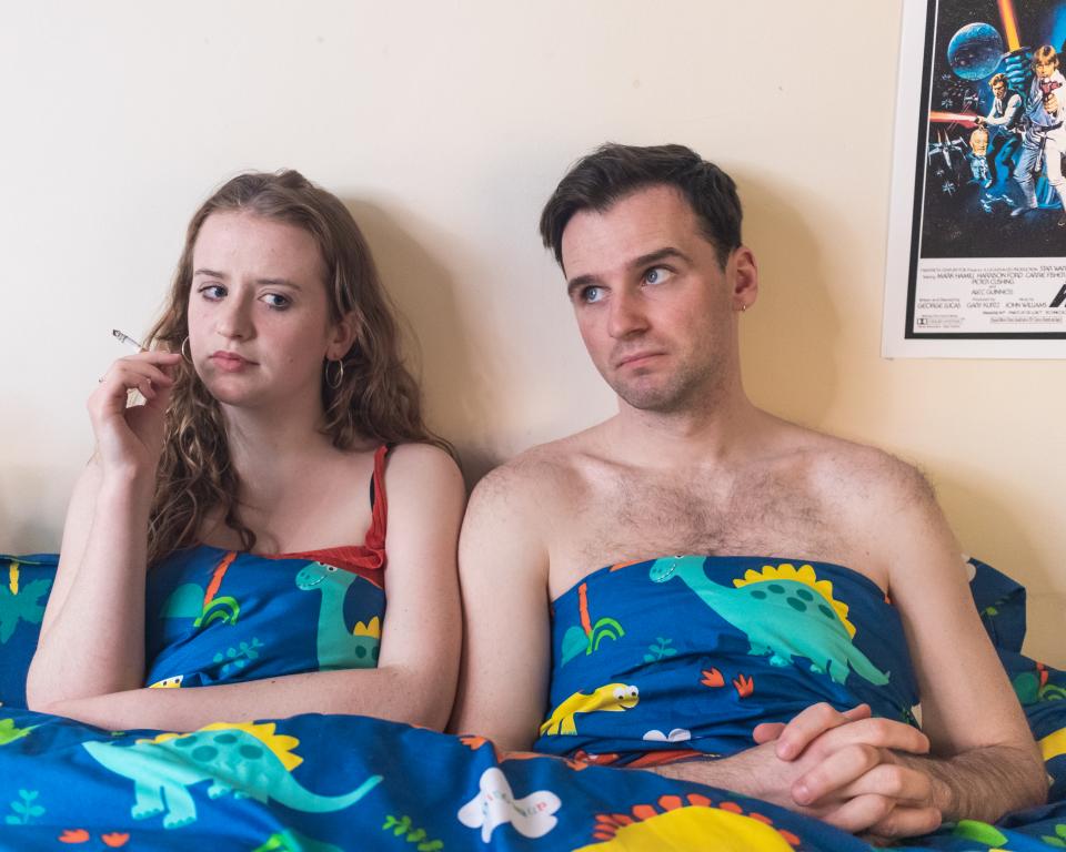 Image of a young woman smoking in bed next to a young man