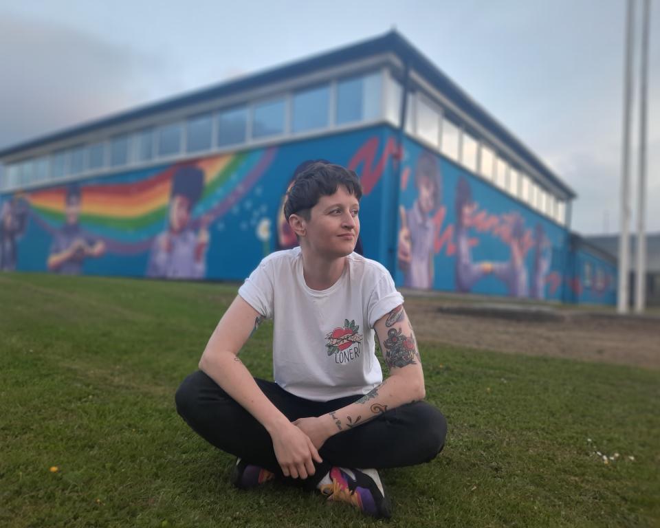 Portrait of artist Emmalene Blake sitting on the grass in front of her mural