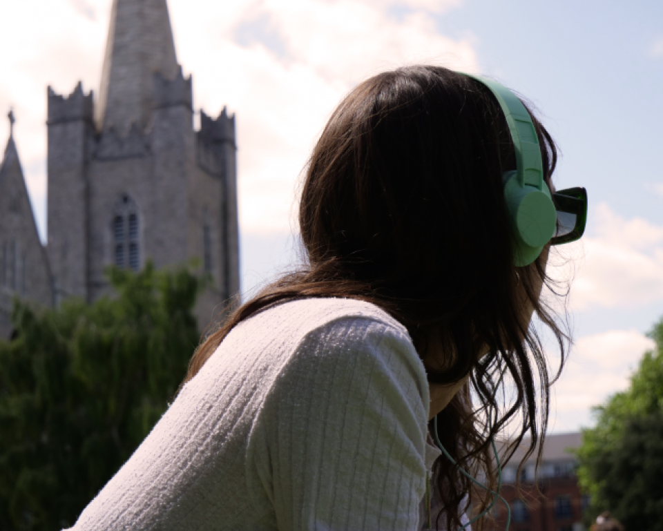 Woman lying in a park with headphones on and a church spire in the background