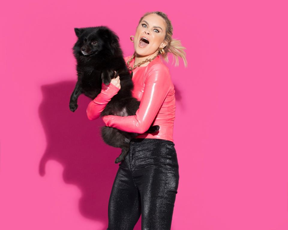 Image of Joanne holding a black dog against a pink background