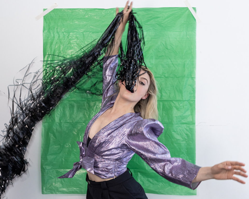Dancer in front of green background swallowing handful of black ribbons