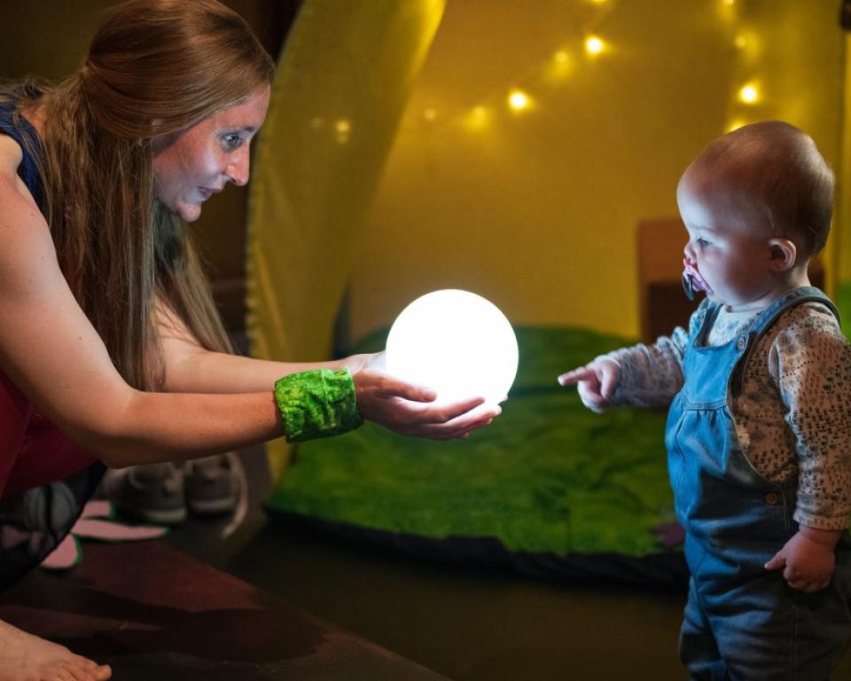 A woman crouching and holding an illuminated globe as a baby touches their finger to it
