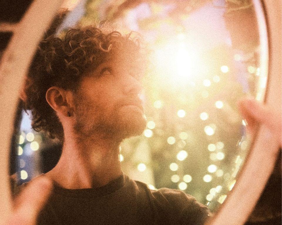A man with curly hair gazes into a mirror, reflecting on his appearance.