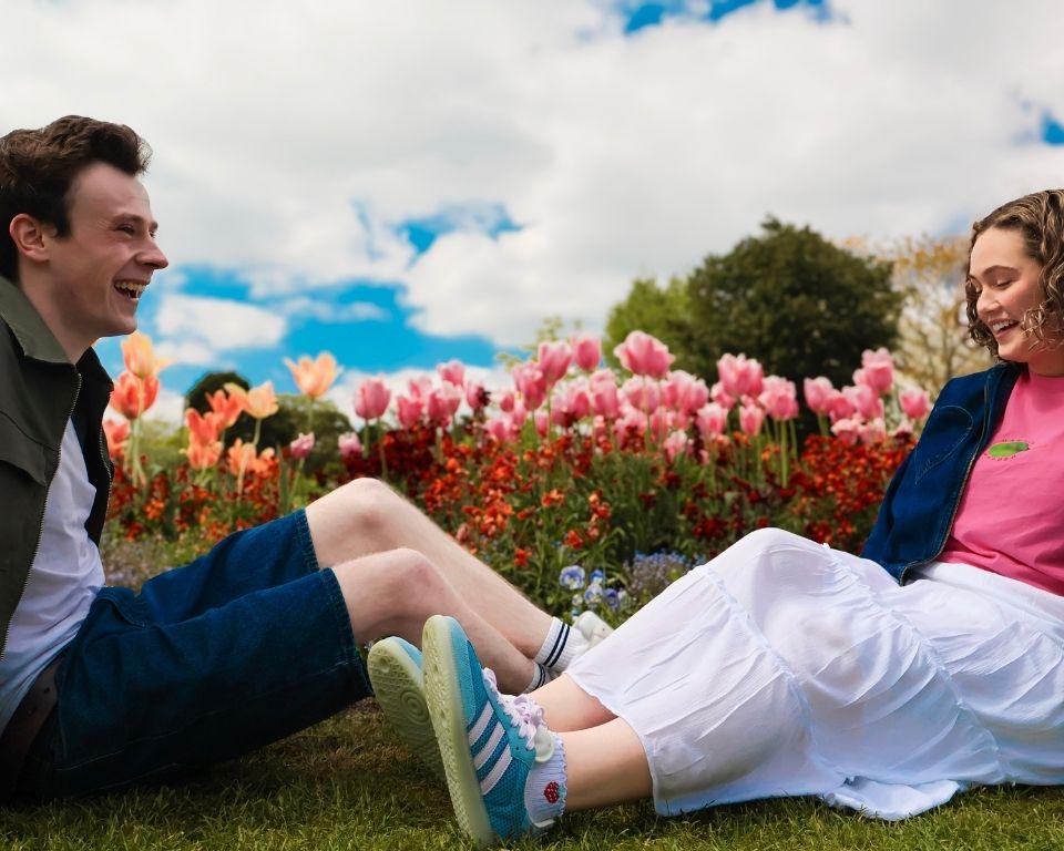 A couple enjoys a moment on the grass, facing a beautiful field filled with blooming tulips.