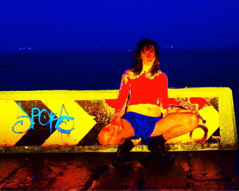 A woman is seated on a bench featuring vibrant graffiti, set against a city backdrop.