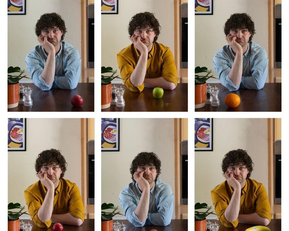A man at a table with an array of colorful fruits, appearing deep in thought or reflection.
