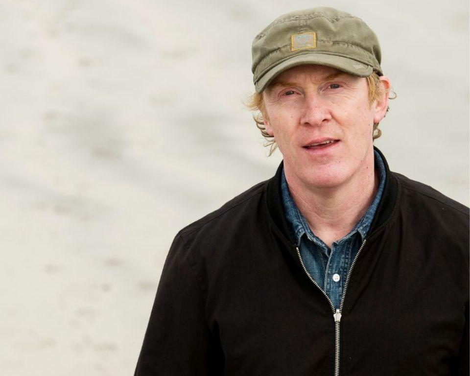 a headshot of the artist in a hat and jacket.