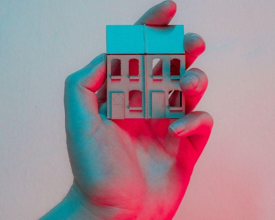A person gently holds a small house in their hand, symbolizing care and ownership.