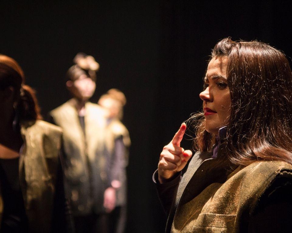 Two women, one in focus are using sign language, against a dark background
