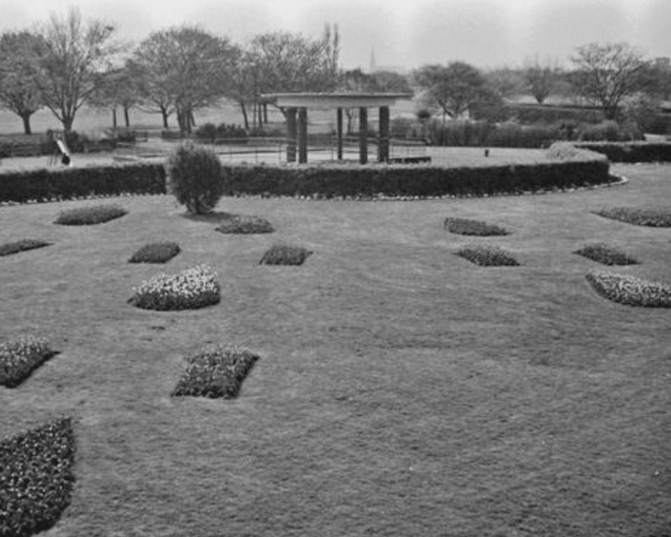 A black and white image showcasing a garden with a gazebo at its center, framed by various plants and trees.