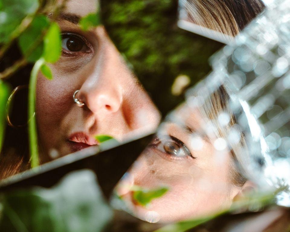 A womans face reflected in shattered glass scattered on top of grass.