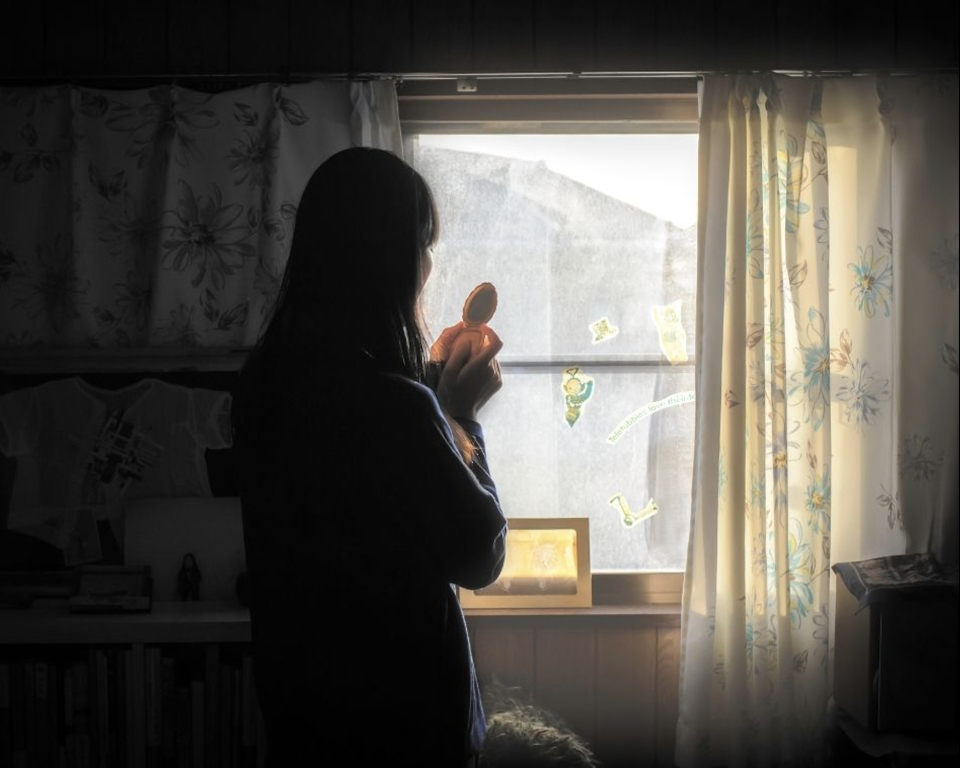 A woman gazes out a window holding an object