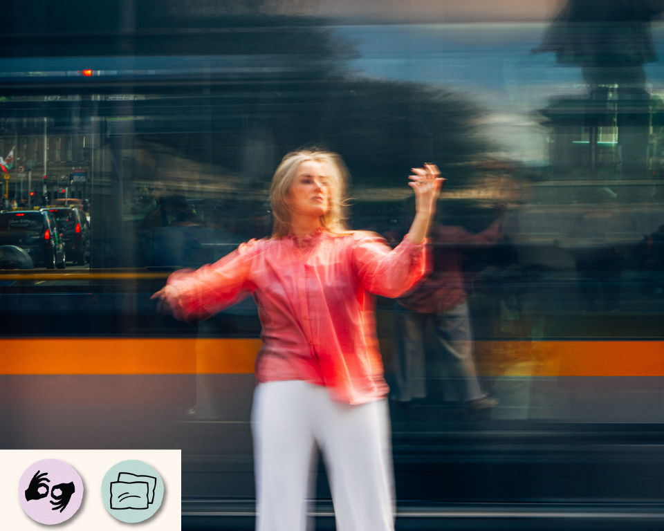 A performer in a coral top stands in front of a moving tram, blurred by motion. Visible access symbols: ISL and Relaxed Performance.
