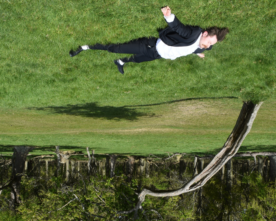 A performer appears to float sideways above a grassy landscape, with the image turned upside down.