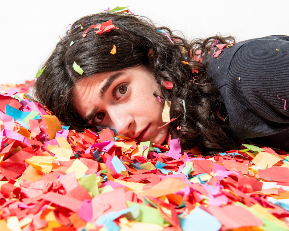 A close-up of a person lying in colourful confetti, looking toward the camera.
