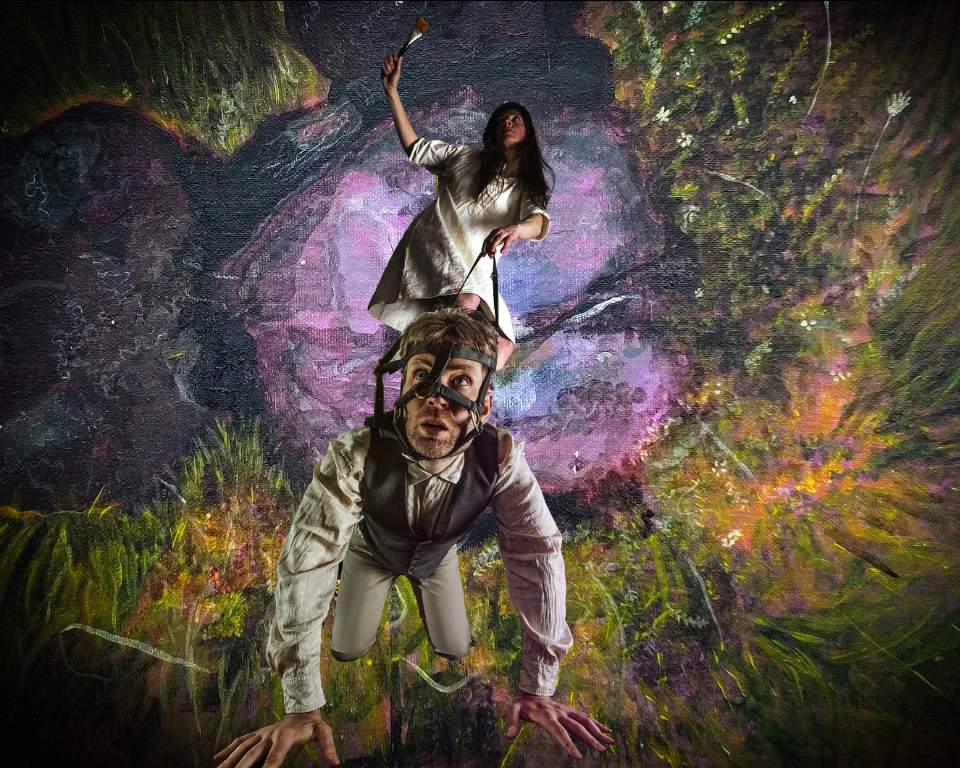 A dancer in a red dress and dark jacket appears doubled and mirrored against a misty landscape. 