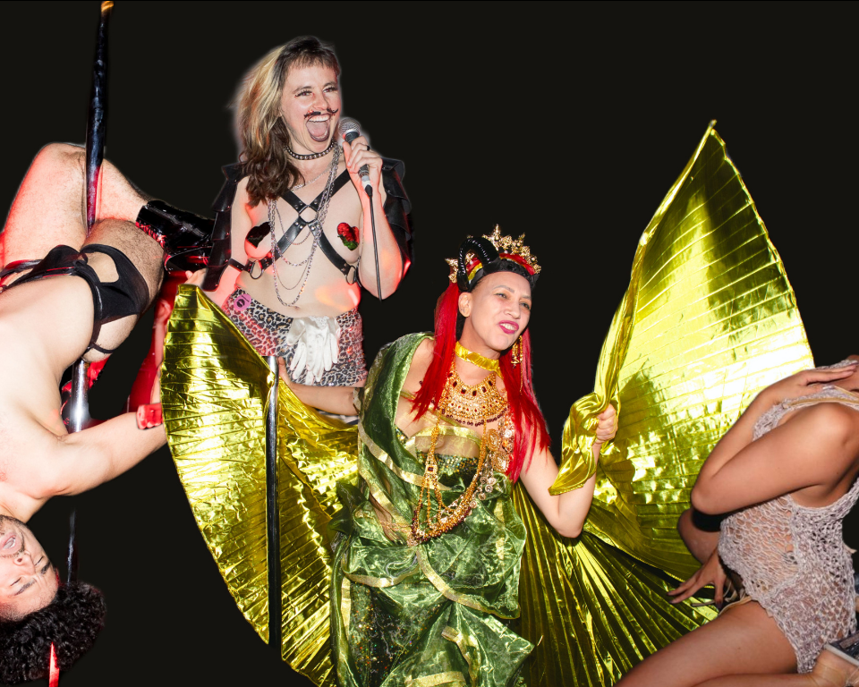 A person with long red hair wearing a metallic green costume and headpiece dances. A second person wearing a leather harness and heart shaped nipple covers sings into a microphone. Two other individuals are seen dancing in the corners of the image. 