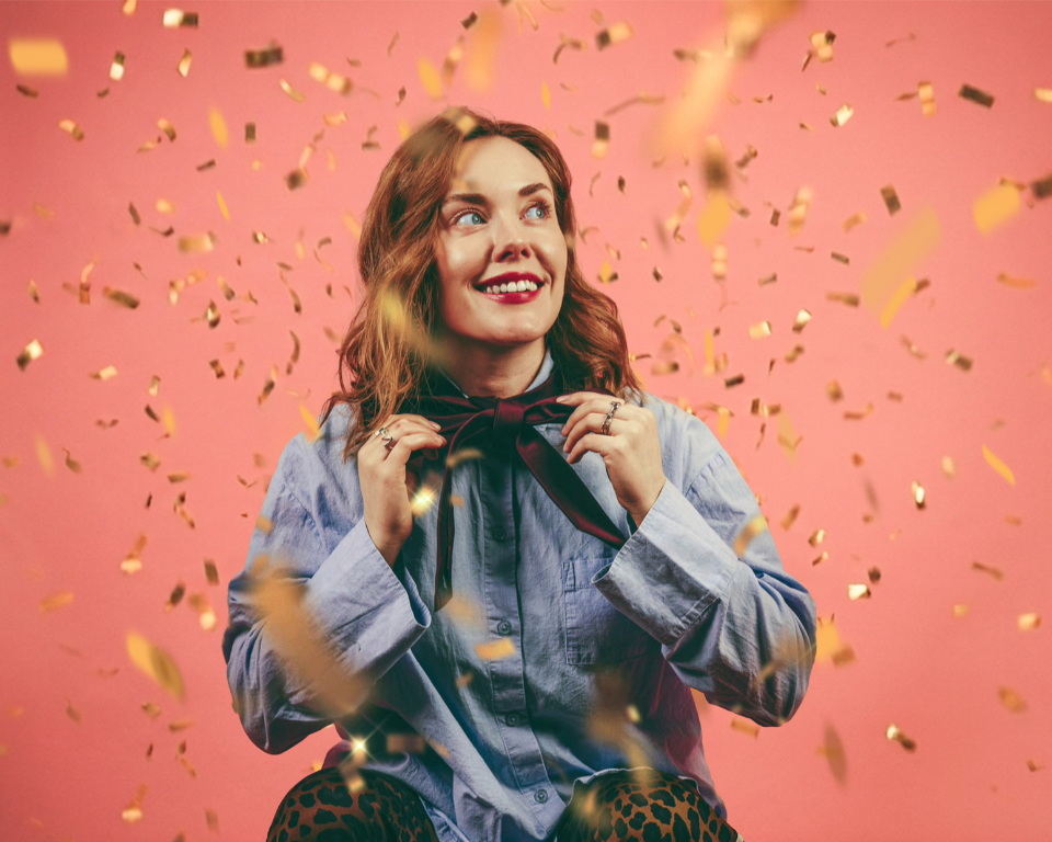 Image of a smiling  woman in front of a peach background with confetti floatting