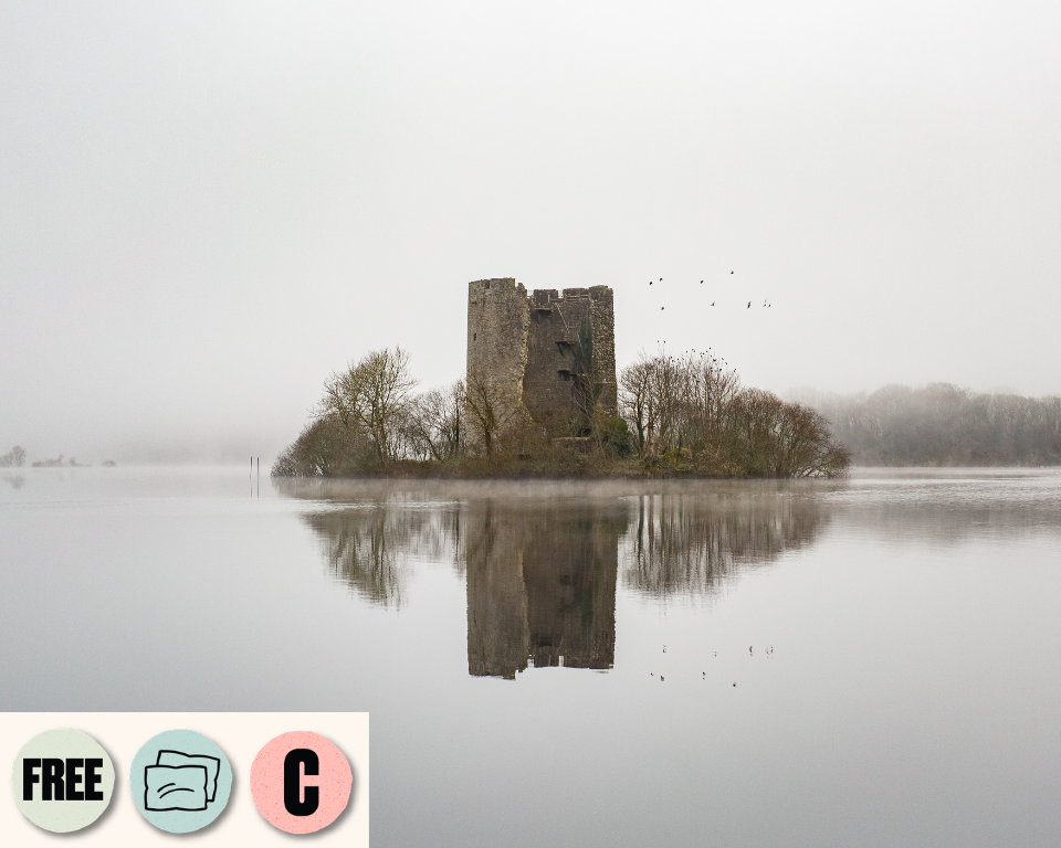 A misty lake surrounds a small island with an old stone tower reflected in the water. Visible access symbols: Creative Captions, Relaxed Performance and Free.