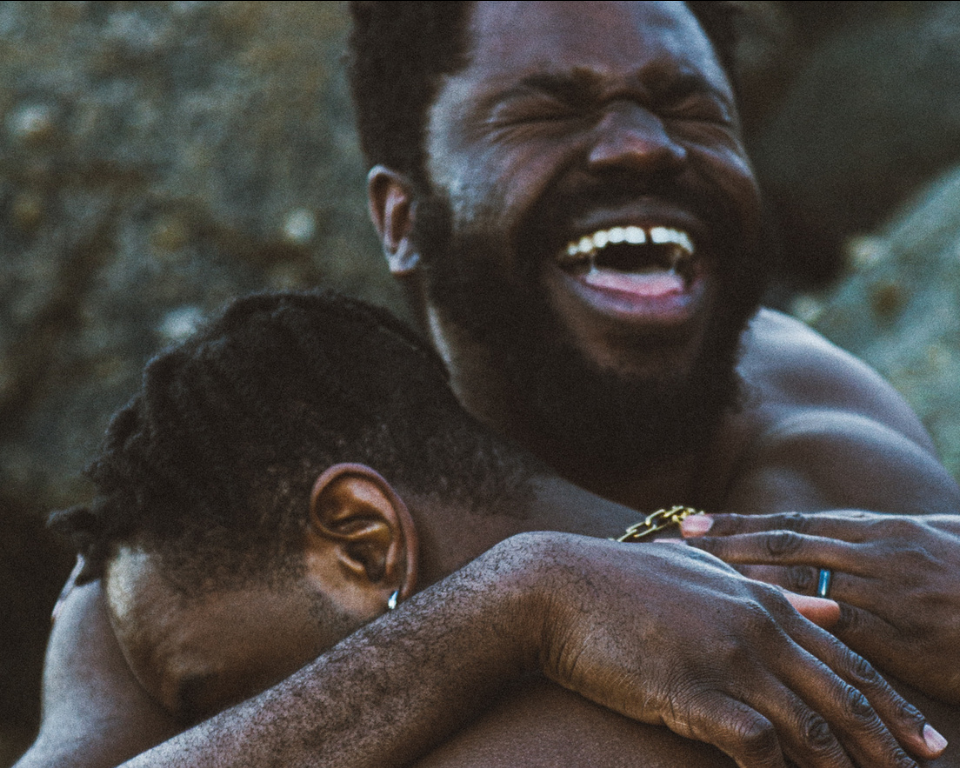Two men embracing in a hug with a wide smile. 