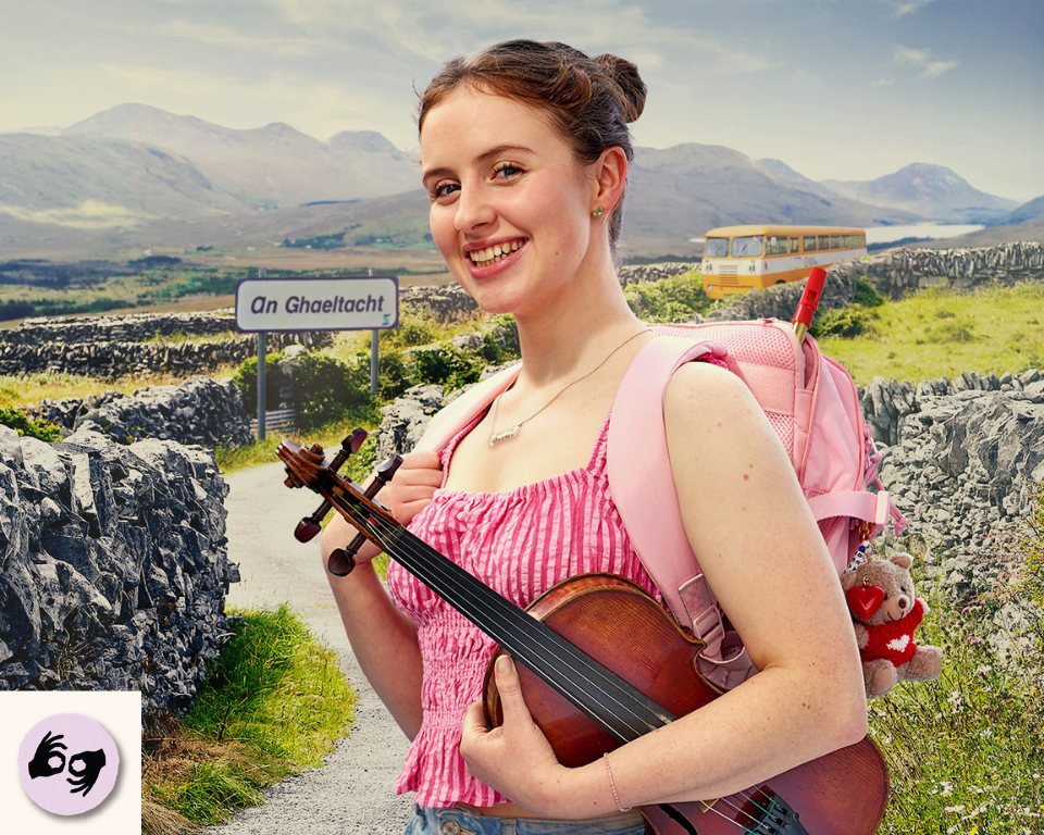 A smiling person wearing a pink backpack holds a fiddle while standing on a rural path lined with stone walls next to an "An Ghaeltacht" road sign. Visible access symbol: ISL
