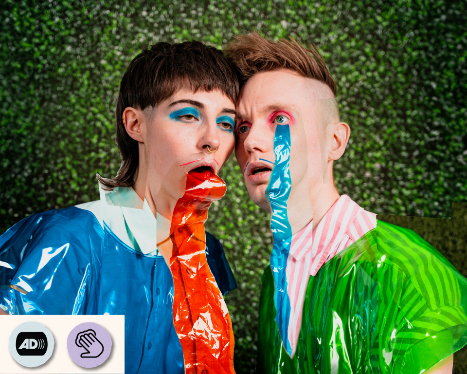 Two performers in shiny blue and green outfits pose close together with bright coloured streamers in their mouths. Visible access symbol: Touch Tours and Audio Description.