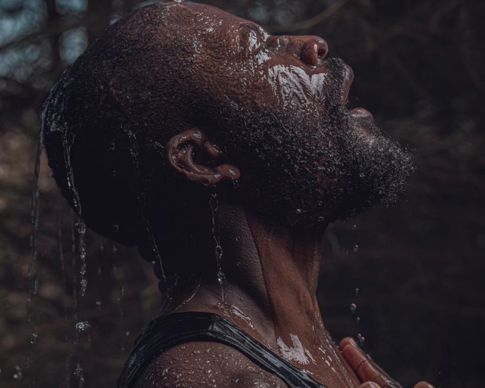 A close-up profile of a person with water running over their face and head against a dark background.