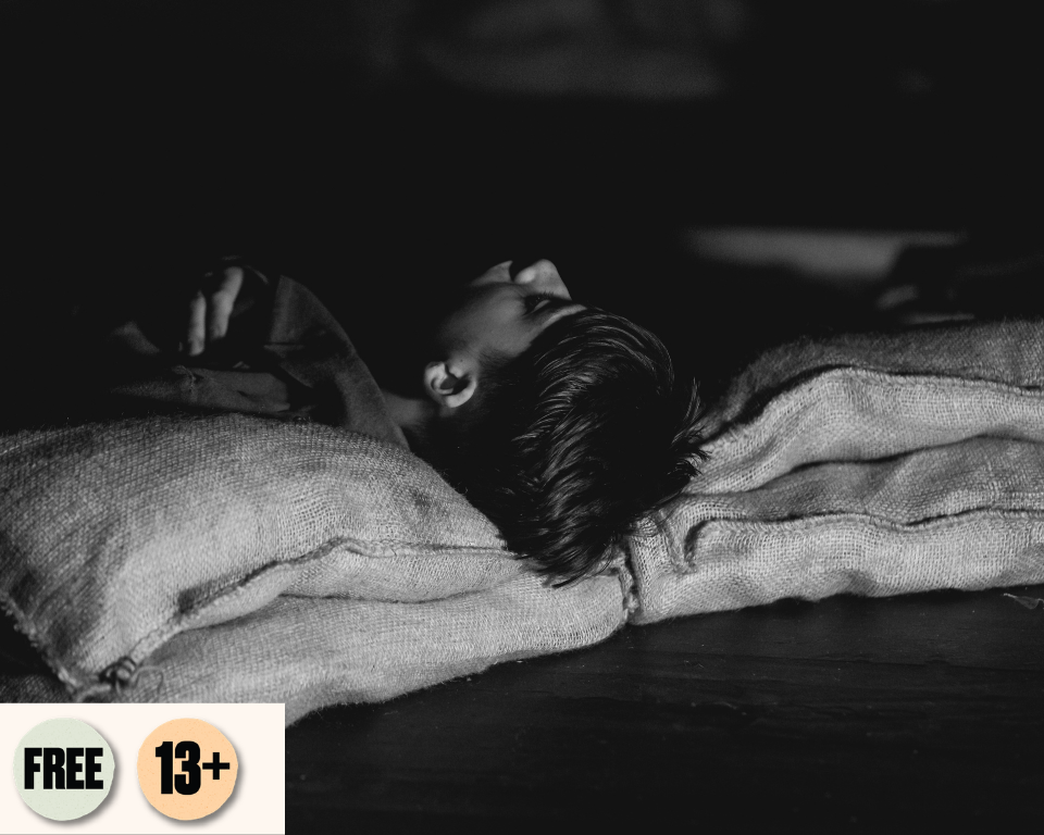 A black and white close-up photo of an child lying down with their head resting on coarse burlap sacks in dim lighting.Visible access symbol: Free and 13+.