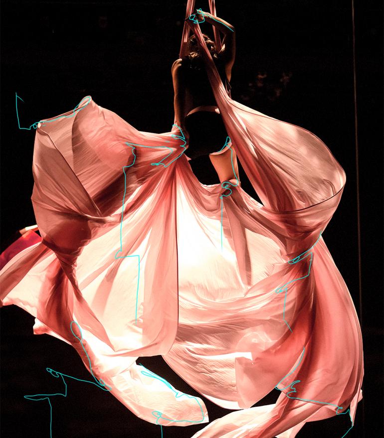 Sorry Gold, a woman hangs from an aerial silk with pink fabric billowing below her
