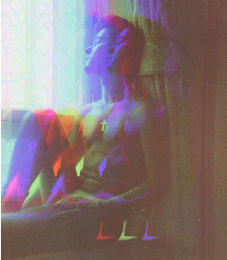A distorted image of a man sitting in a window sill with a cross necklace