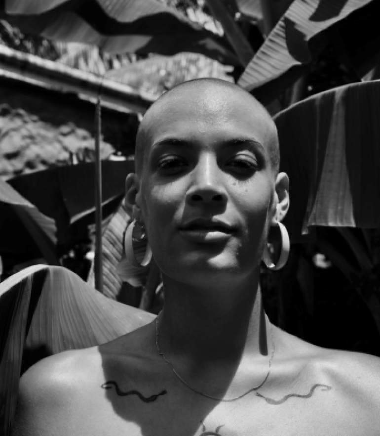 Black and white image of a person with bare shoulders, big looped earrings and shaved head. 