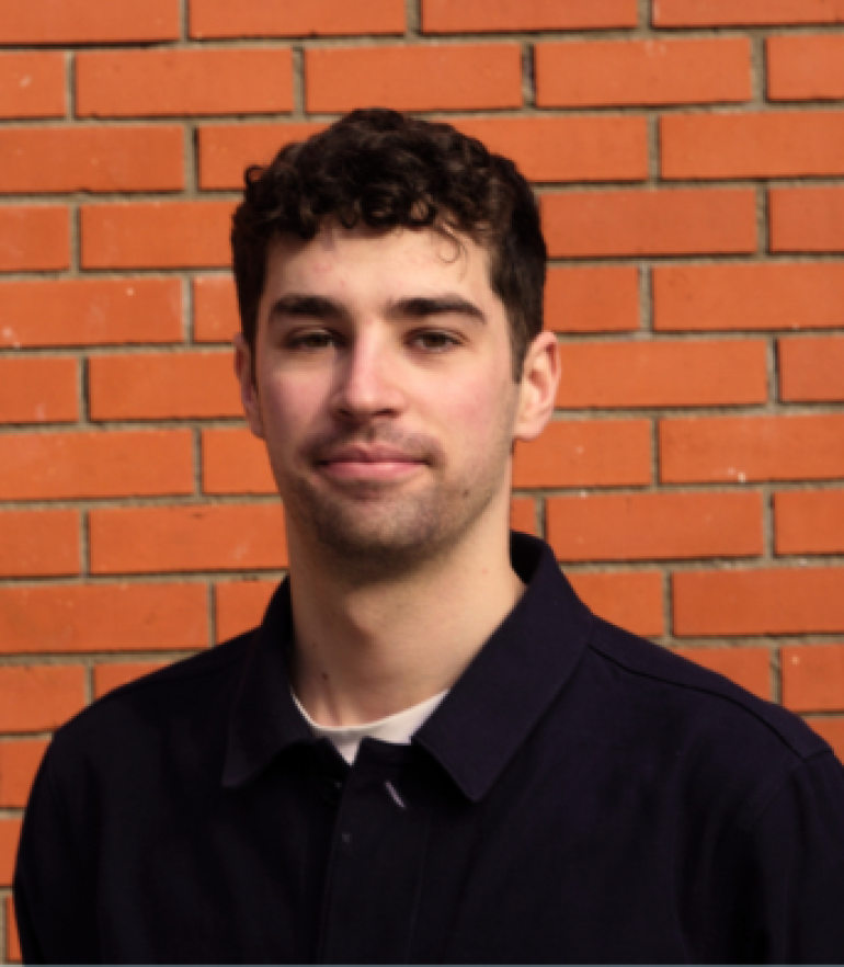 Danny Kendrick: Portrait of Danny Kendrick standing in front of a red brick wall, wearing a dark navy shirt.