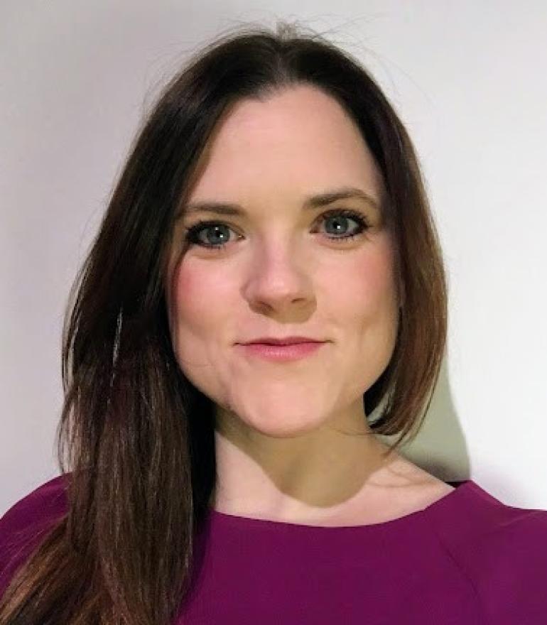 a white woman in a purple dress with brown straight hair smiles to the camera