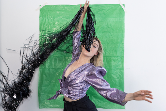 Dancer in front of green background swallowing handful of black ribbons