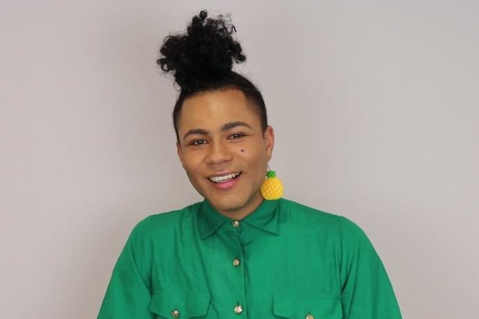 Portrait of Travis Alabanza smiling with green shirt and pineapple earring
