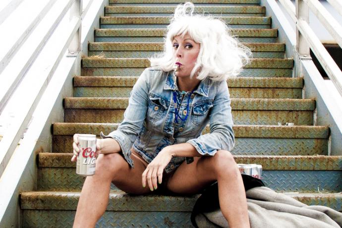 Performer Adrienne Truscott sitting on outdoor steps with a whistle and can of beer