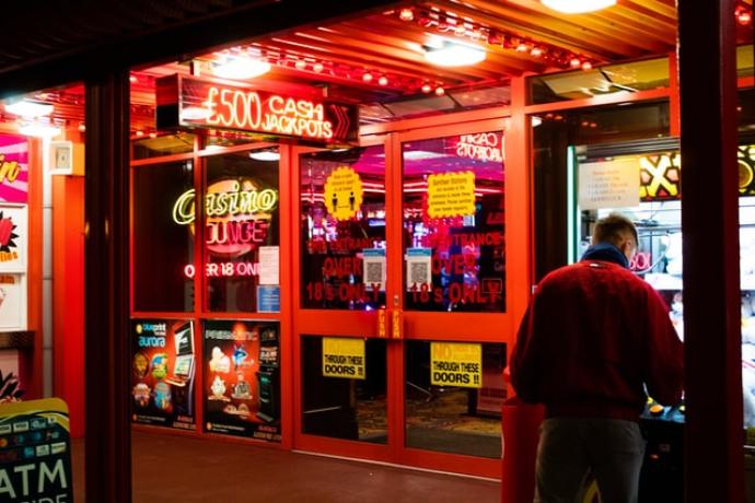 A male figure standing outside a casino in front of red neon lights