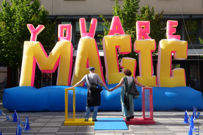 A couple hugging in front of an inflatable artwork reading 'You Are Magic'
