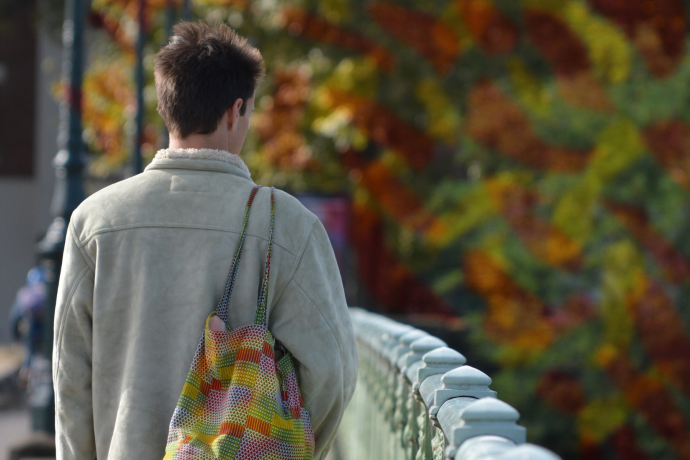 A person facing away walks over a bridge with a bag slung over their shoulder.. 
