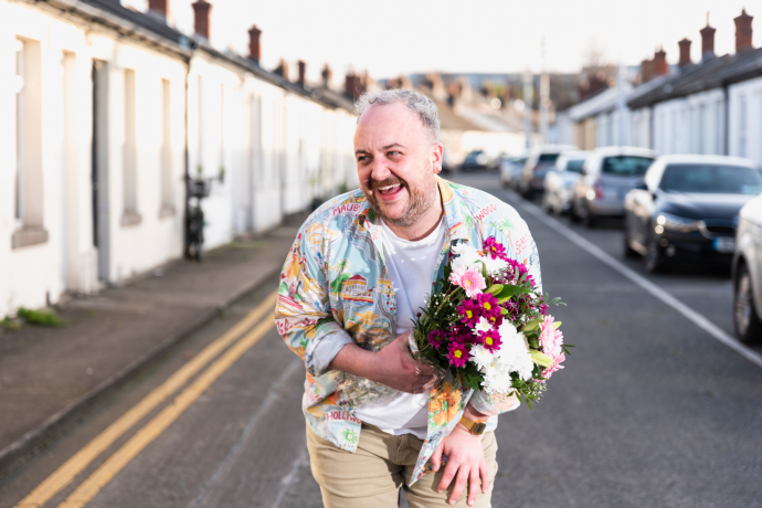A man holding a bunch of flowers in the middle of a street of terraced houses