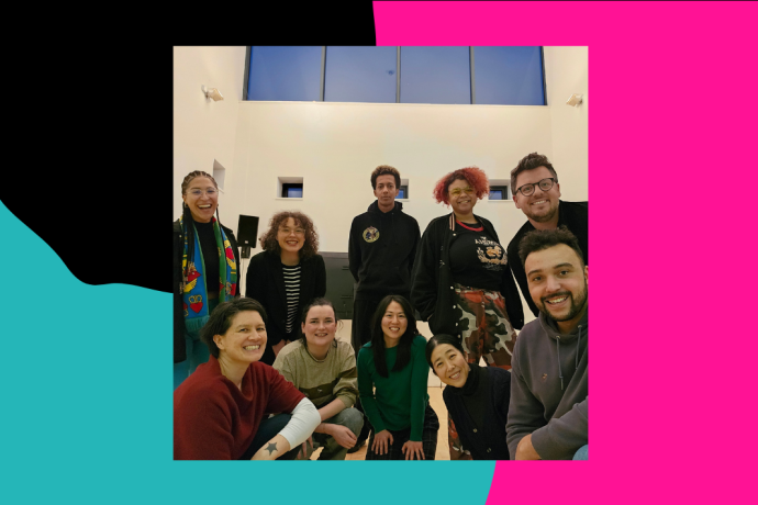 A group of ten people pose for the camera. Five stand behind the rest of the group who are hunkering down to get in shot. They are in a rehearsal room.