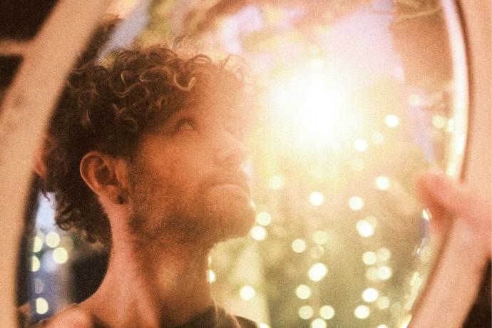 A man with curly hair gazes into a mirror, reflecting on his appearance.